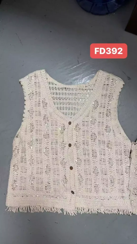 A flat lay of a cream-colored crochet vest featuring buttons and fringe detail at the hem.
