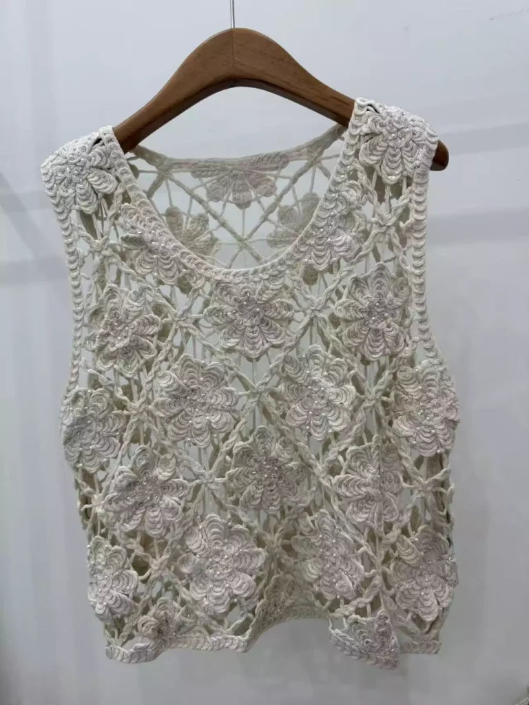 A hanger shot of a white floral crochet tank top, showcasing intricate handmade flower patterns and delicate openwork design.
