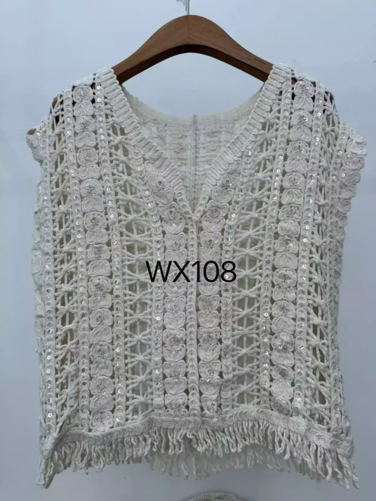 A hanger shot of a white geometric crochet vest, featuring sequin embellishments and a fringe hem, style WX108.