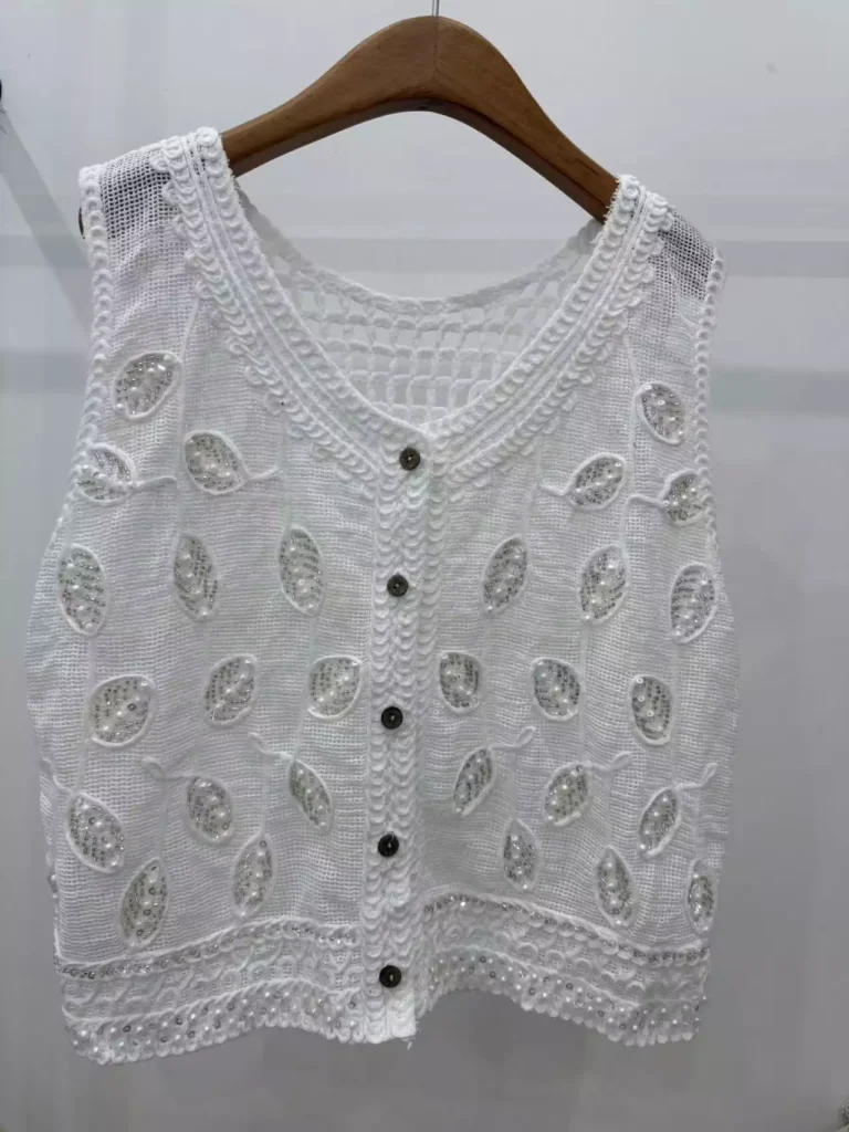 A hanger shot of a white leaf-pattern crochet vest, showcasing pearl and sequin details, and button-front design.