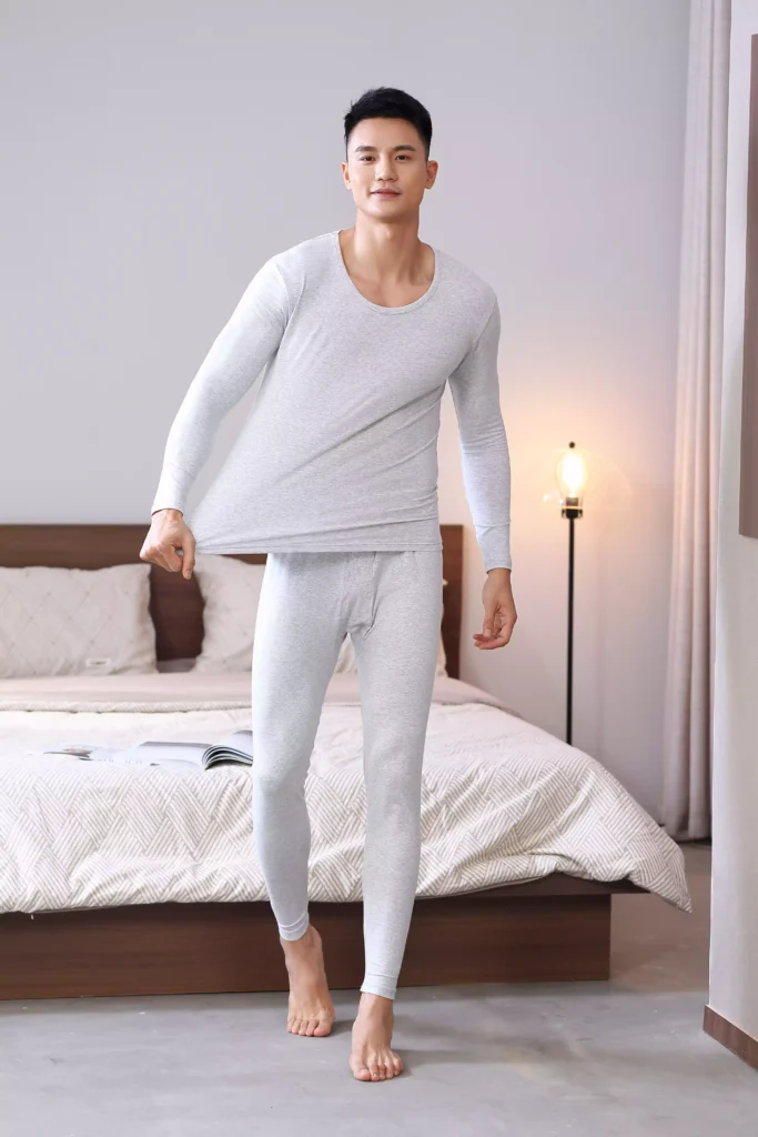 A man demonstrating the stretchability and elastic fit of a grey thermal underwear set, highlighting the flexible fabric quality.