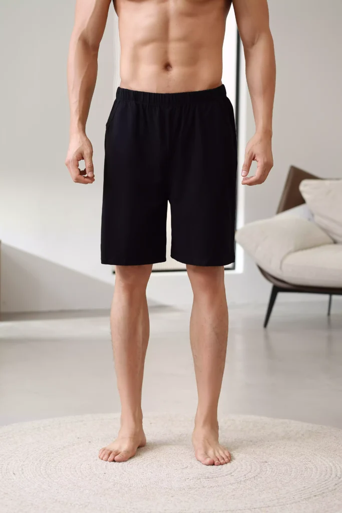 Front view of a man wearing comfortable black lounge shorts, standing on a circular rug in a minimalist home setting.