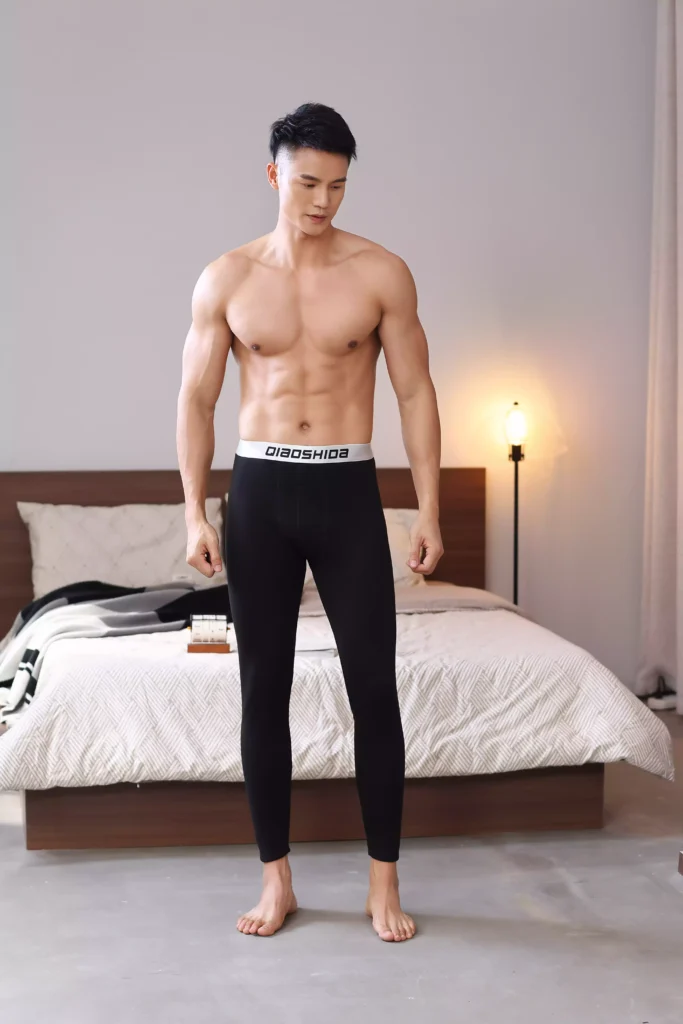 Full-body view of a muscular man wearing black compression leggings with a branded waistband.