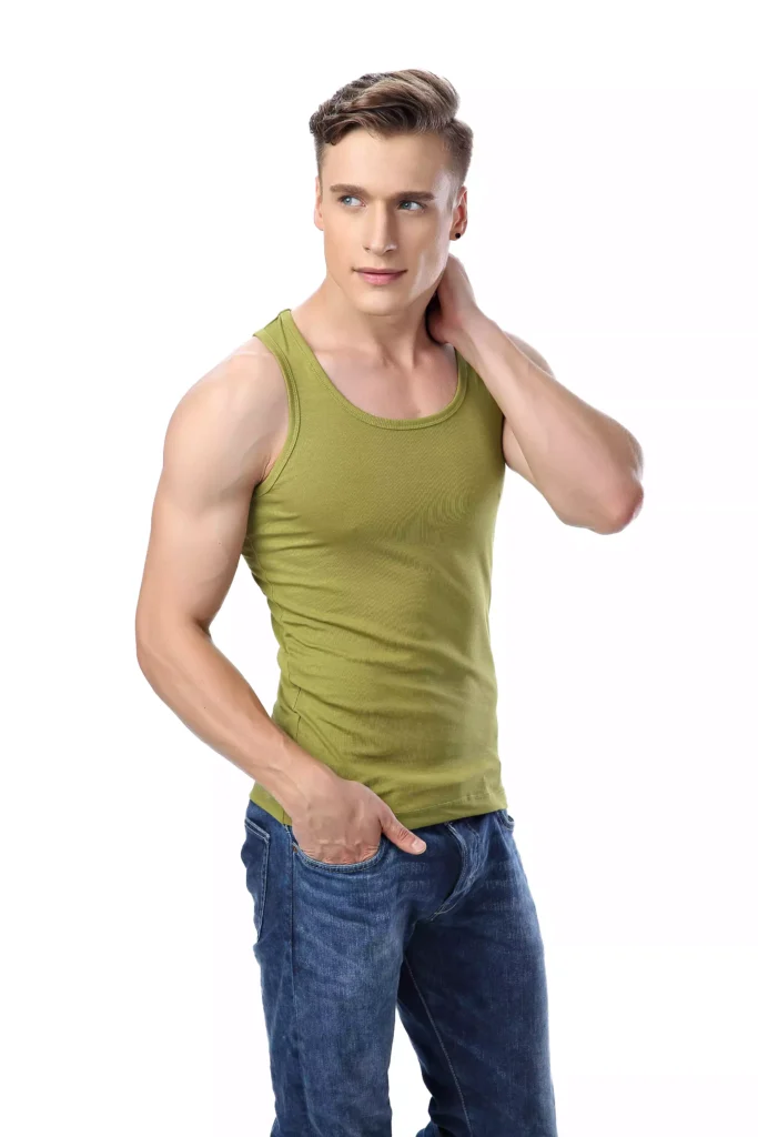 A fit man posing in a stylish olive green tank top and blue jeans, standing against a white background.