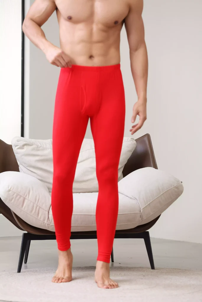 Man adjusting the elastic waistband of red thermal leggings, showing the comfortable fit and flexible fabric quality.