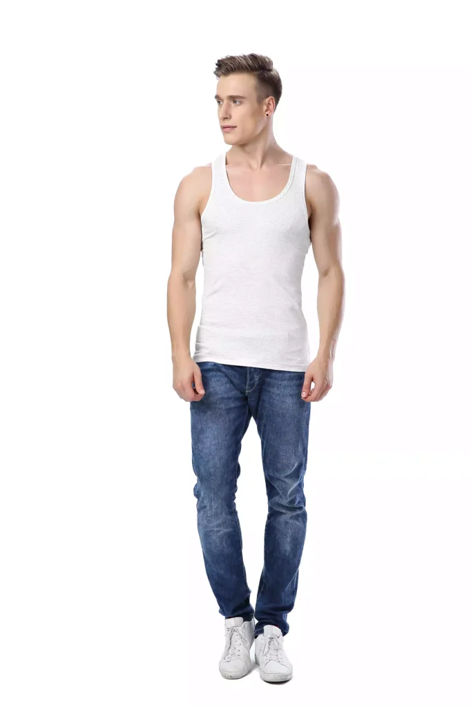 A fit man standing against a white background, wearing a casual white tank top and blue jeans.