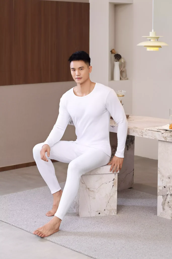 A man sitting down wearing a white thermal underwear set, showcasing the comfort and flexibility of the fabric.