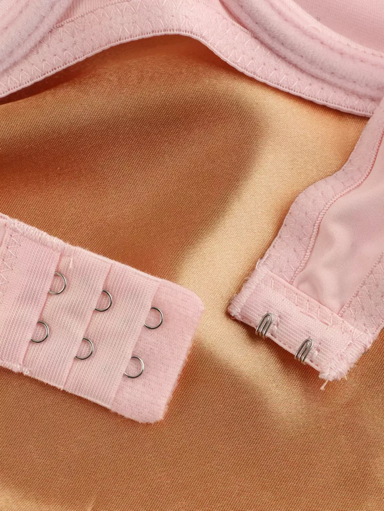Close-up of the hook-and-eye closure on a light pink bra, showing the sturdy metal fasteners and soft fabric construction.