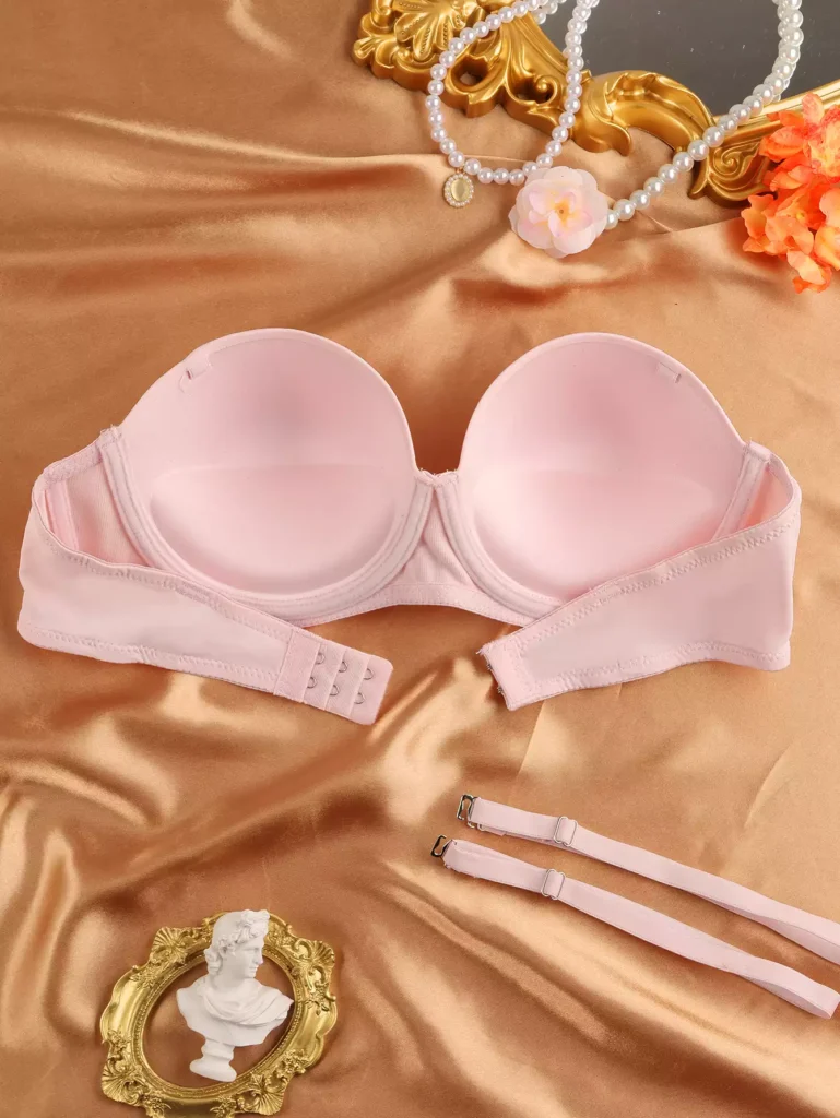Flat lay view of a light pink strapless bra showing inner padding, molded cups, and detachable shoulder straps on a silk background.