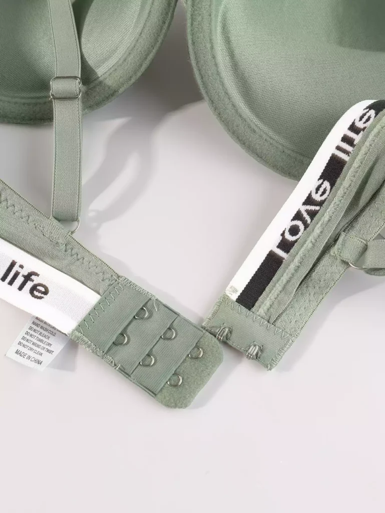 Close-up view of a sage green bra showing the adjustable hook-and-eye closure, branded elastic band, and care instructions label.