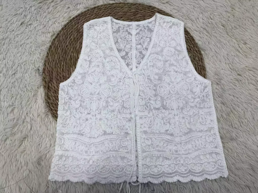 A flat lay of a white floral embroidery crochet vest, showcasing intricate openwork textures and handcrafted details.