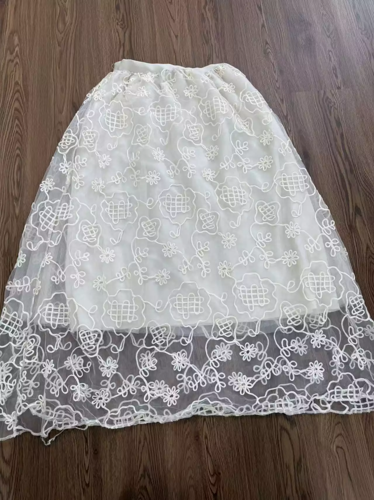A flat lay of a white mesh maxi skirt featuring exquisite floral embroidery, showcasing an elegant and detailed texture.