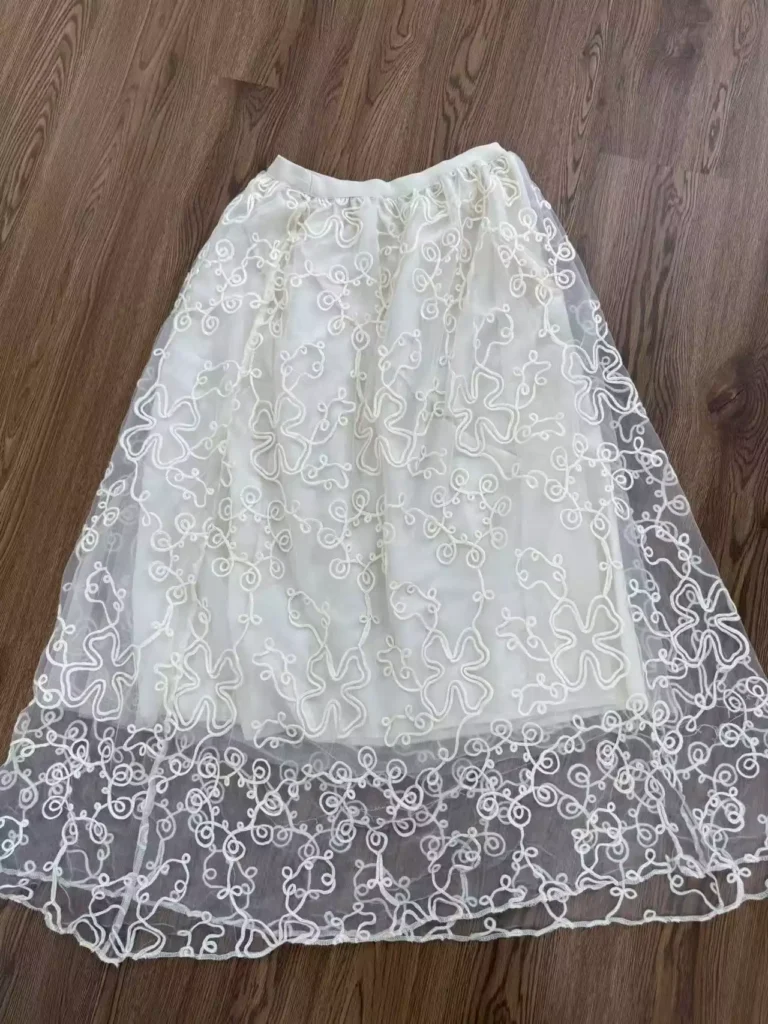 A flat lay of a white mesh lace maxi skirt featuring exquisite swirl-pattern embroidery, showcasing an elegant and ethereal aesthetic.