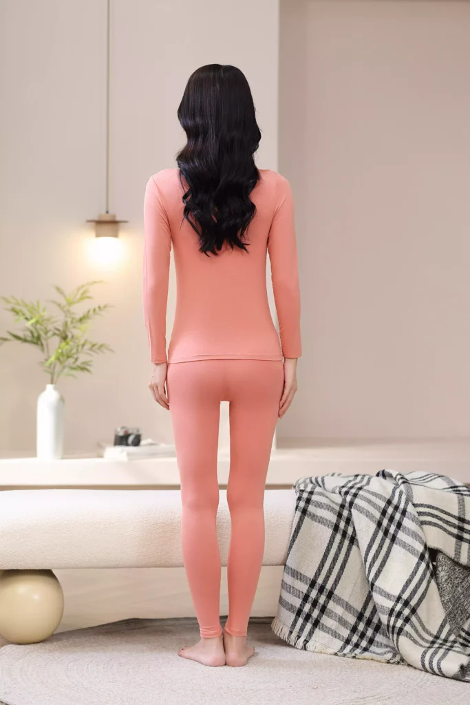 Back view of a woman wearing a coral pink thermal underwear set, showcasing the sleek, slim-fit design and comfortable cut of the long-sleeve top and leggings.