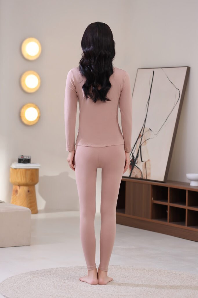 Back view of a woman wearing a dusty pink thermal underwear set, showcasing the sleek, slim-fit design of the top and leggings.