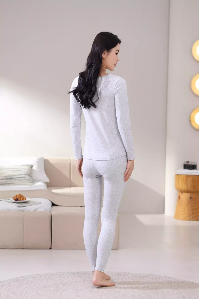 Back view of a woman wearing a grey thermal underwear set, showcasing the sleek, slim-fit design and comfortable cut of the long-sleeve top and leggings.