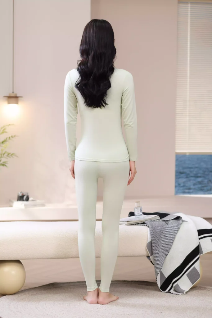 Back view of a woman wearing a light green mock-neck thermal underwear set, showcasing the sleek, slim-fit design and comfortable cut of the long-sleeve top and leggings.
