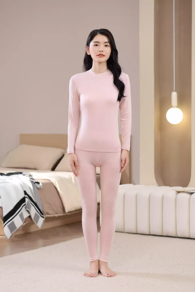 Front view of a woman wearing a pink mock-neck thermal underwear set, featuring a long-sleeve top and leggings with a slim-fit design in a cozy bedroom setting.