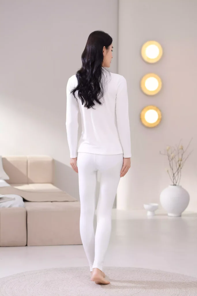 Back view of a woman wearing a white mock-neck thermal underwear set, showcasing the sleek, slim-fit design and comfortable cut of the long-sleeve top and leggings.